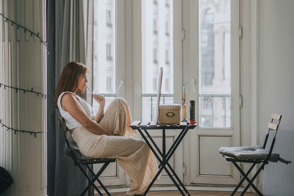 Frau sitzt nachdenklich an einem kleinen Tisch bei hohen Stadtfenstern mit Notizbuch und Kaffee — Flexibilität ist wichtiger, als Sie denken