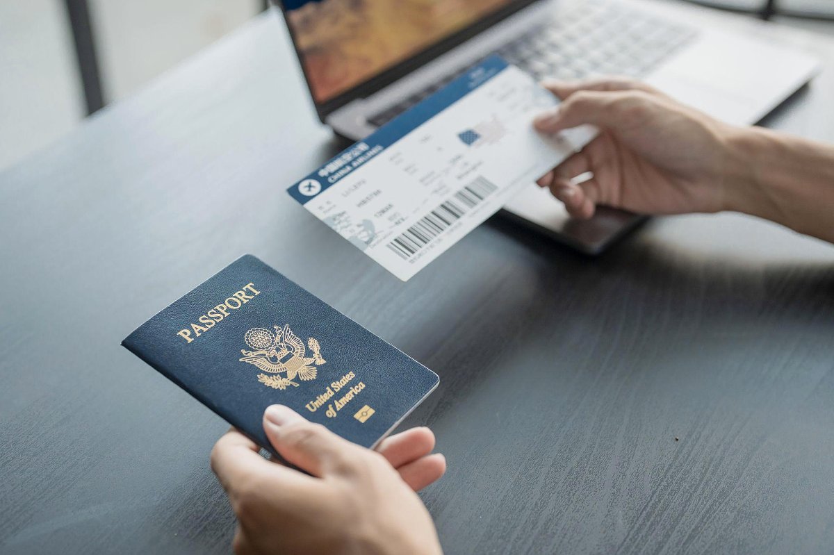 Niroskos-Blog „Wo anfangen...“: US-Reisepass und Bordkarte auf einem Schreibtisch, Hand hält das Ticket neben einem Laptop