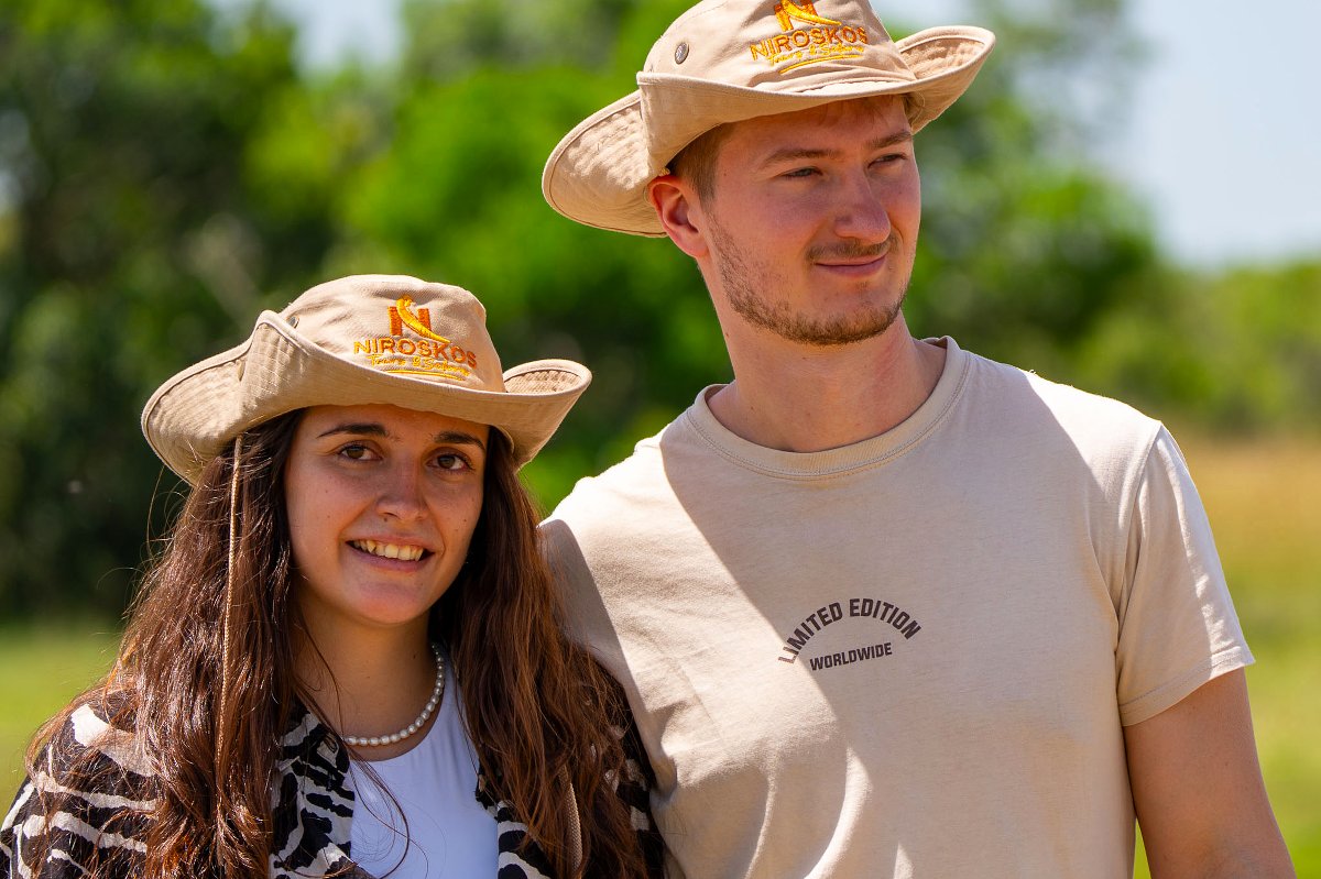 Two tourists wearing Niroskos safari hats smiling in a sunlit African savanna