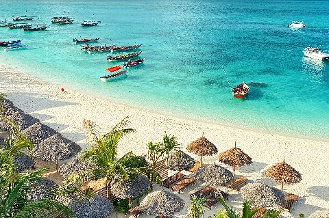 Crystal-clear turquoise reef waters off Zanzibar, showing dark coral patches beneath the surface