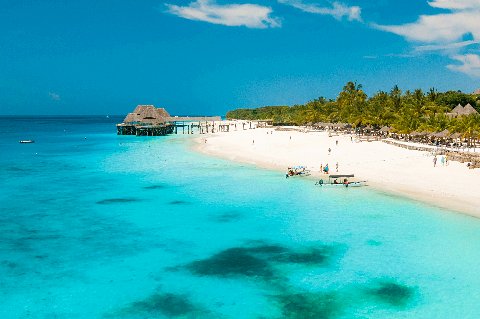 Turquoise water and white-sand beach near Zanzibar City with a wooden pier and moored boats