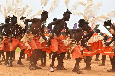 Traditional Ugandan dancers in orange skirts and feathered headpieces performing outdoors
