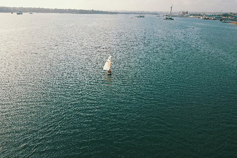 Lone sailboat drifting on calm coastal waters with a distant harbor off Tanzania's shore