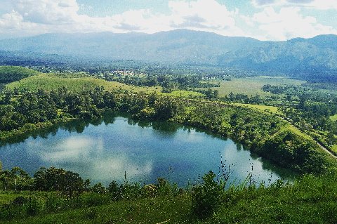 Aerial view of a crater lake surrounded by green rolling hills and distant mountains in Uganda
