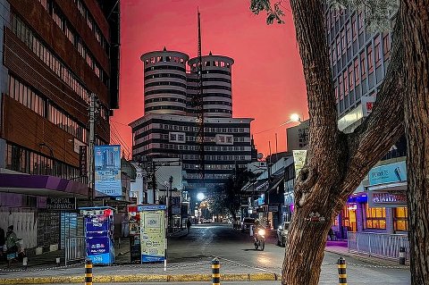 Tree-lined urban street at dusk framed by buildings and two cylindrical towers under a pink sky in Kenya